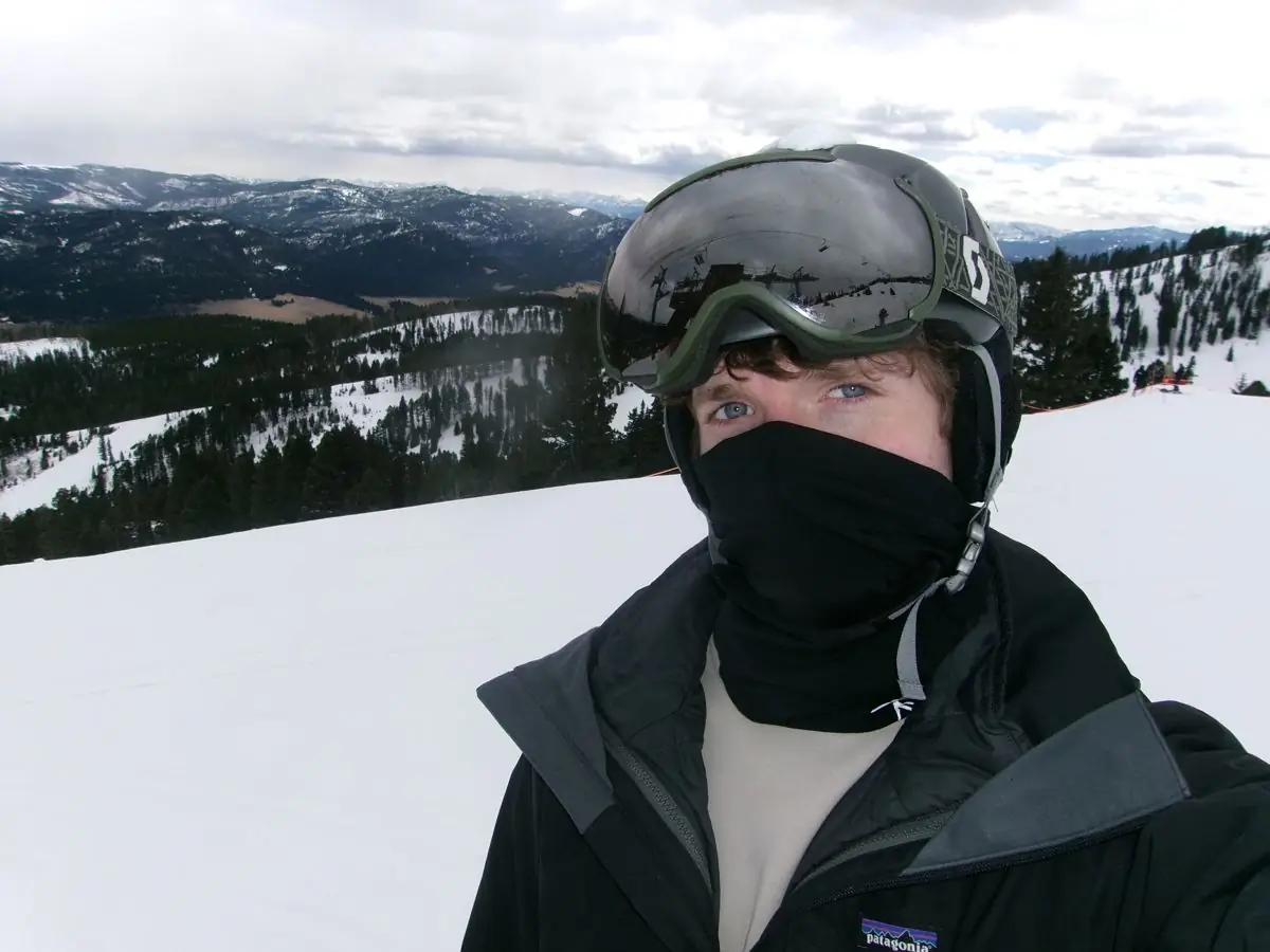 Charlie between runs — goggles up on his helmet, balaclava on, snowy slope behind