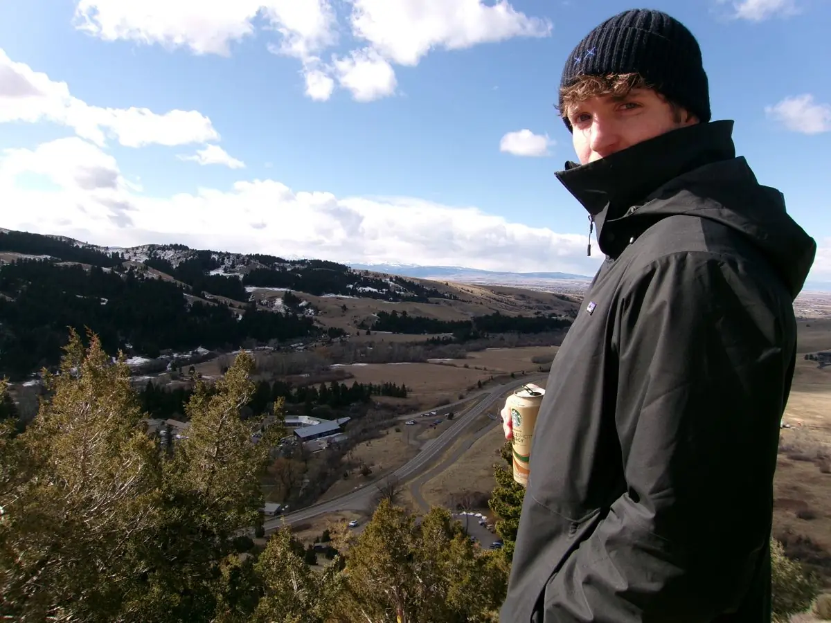 Charlie on a ridge, hands on his beanie, collar up against the wind